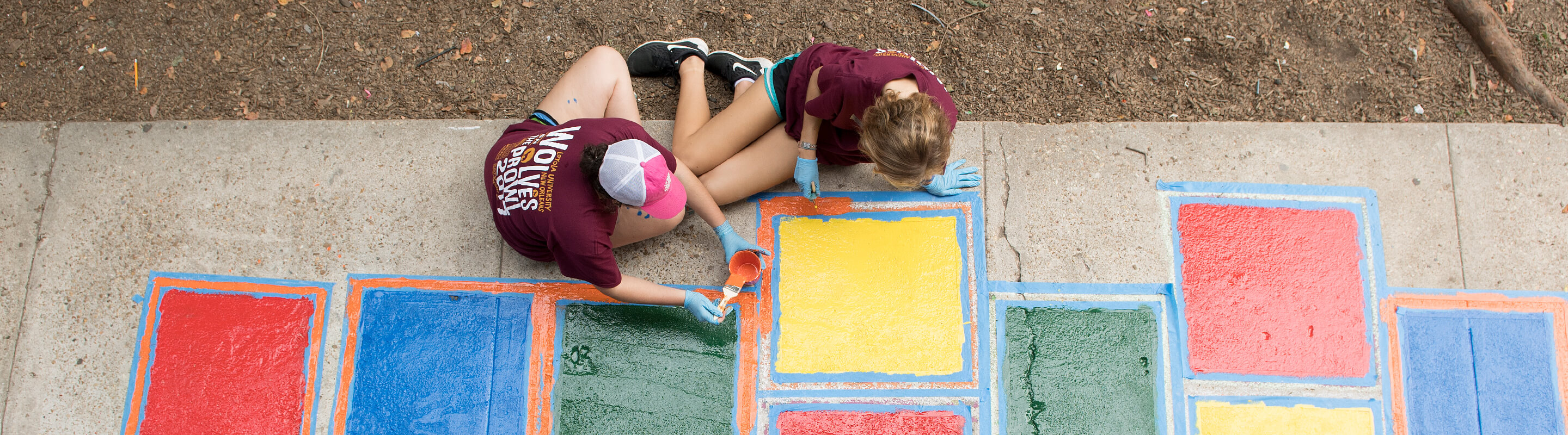 Two alumni painting hopscotch on a sidewalk 