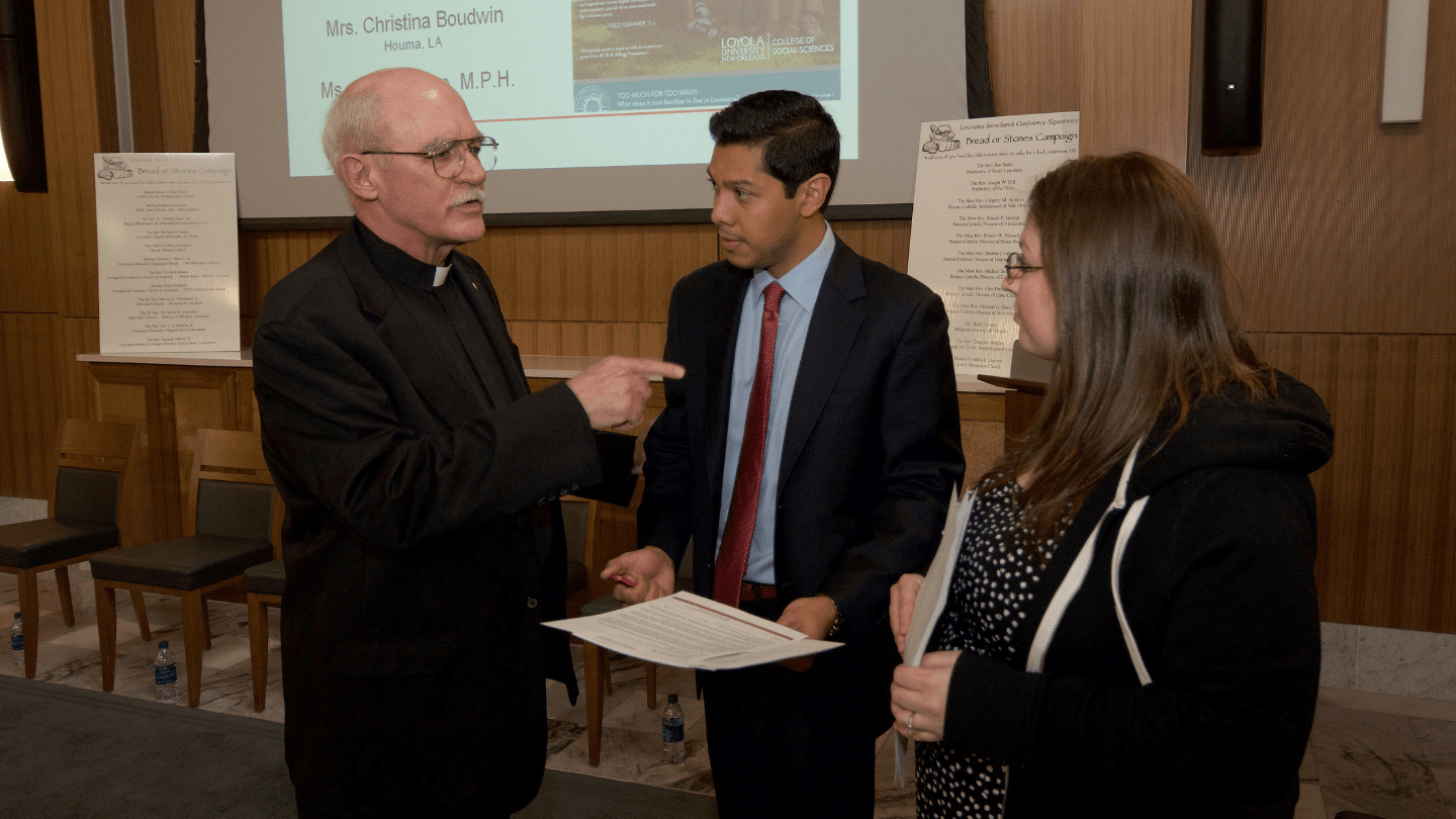 Two students wearing business dress chatting with a professor shortly before presenting on their research.